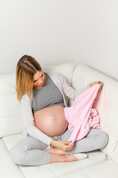 Schwangere Frau, die auf Sofa sitzt und eine Decke betrachtet