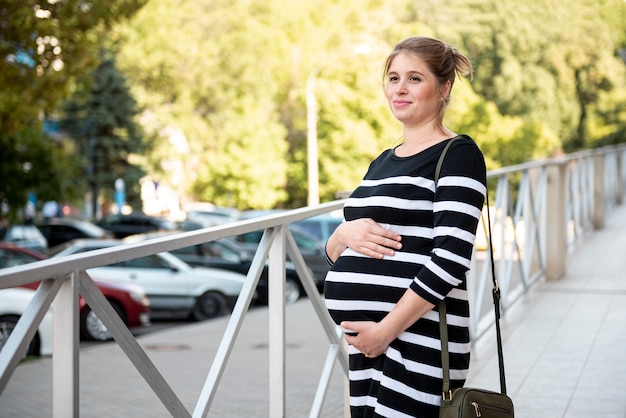 Schwangere Frau, die draußen ihren Bauch hält