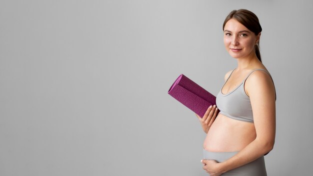 Schwangere Frau, die eine Fitnessmatte mit Kopienraum hält