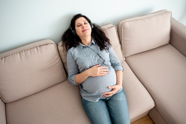 Schwangere Frau, die ihren Bauch berührt und Musik hört