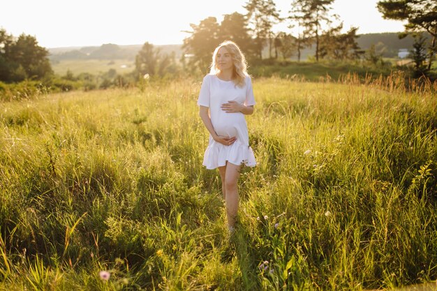 Schwangere Frau, die im Park mit Sonnenuntergang geht