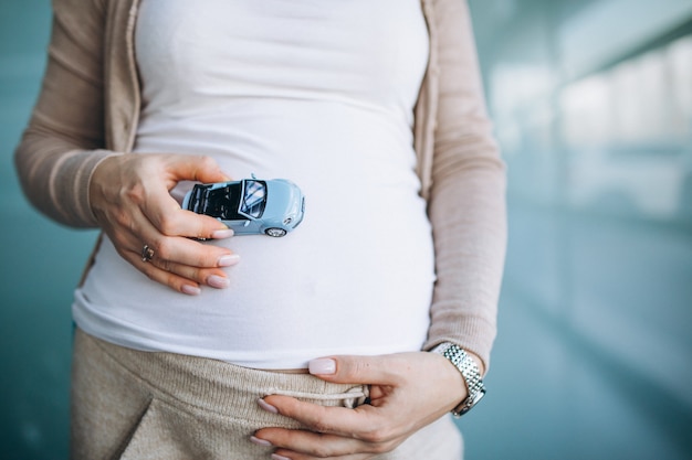 Schwangere Frau, die kleines Automodell durch den Bauch hält