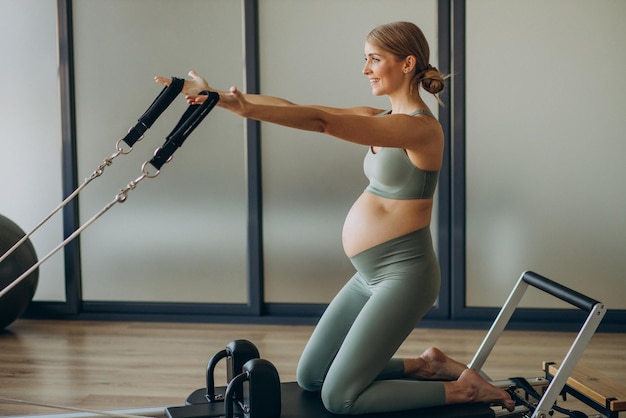 Schwangere frau, die mit hilfe des reformers im pilates-kurs trainiert