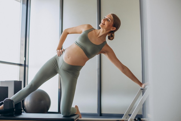 Schwangere Frau, die mit Hilfe des Reformers im Pilates-Kurs trainiert