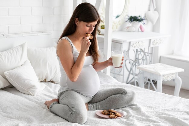 Schwangere Frau, die Schokoladenplätzchen und Trinkmilch isst