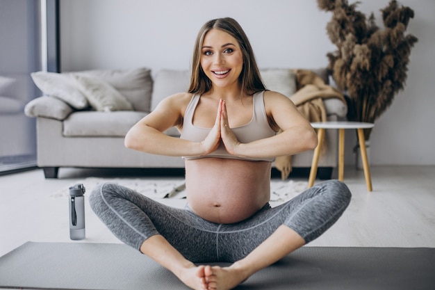 Schwangere frau, die zu hause yoga auf der matte praktiziert