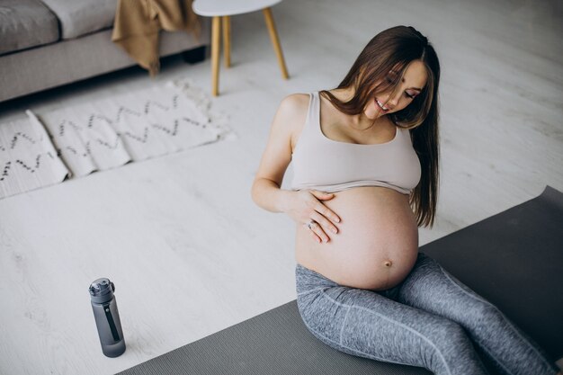 Schwangere Frau, die zu Hause Yoga auf der Matte praktiziert