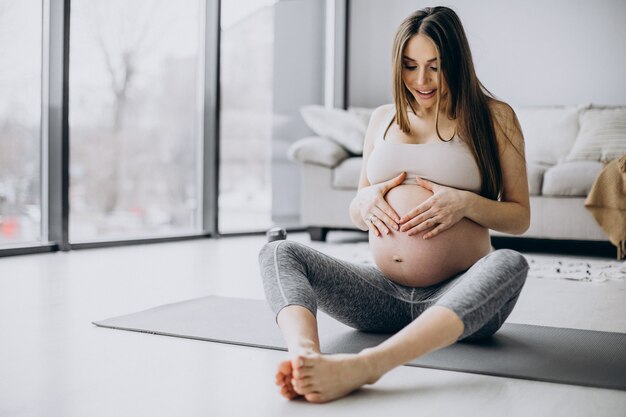 Schwangere Frau, die zu Hause Yoga auf der Matte praktiziert