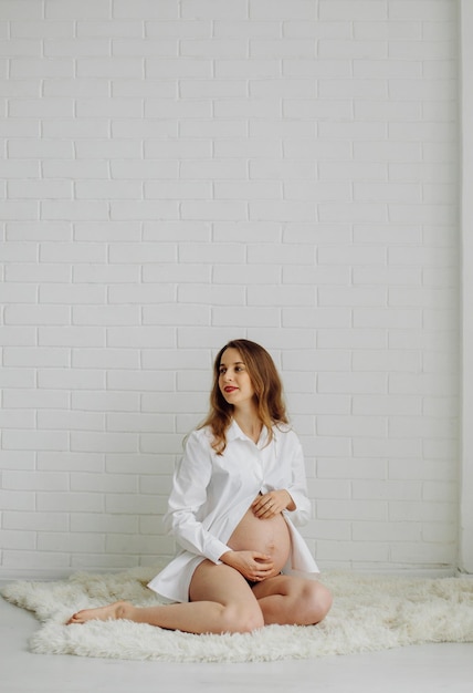 Schwangere Frau im Studio In einem weißen Hemd