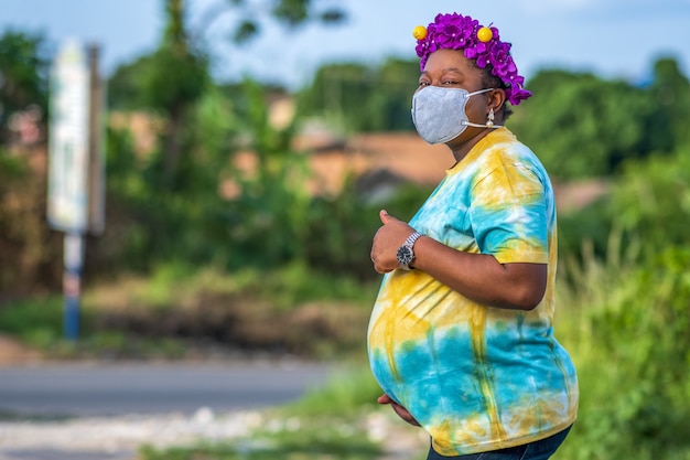Schwangere Frau in einer schützenden Gesichtsmaske, die das Daumen-hoch-Zeichen gestikuliert