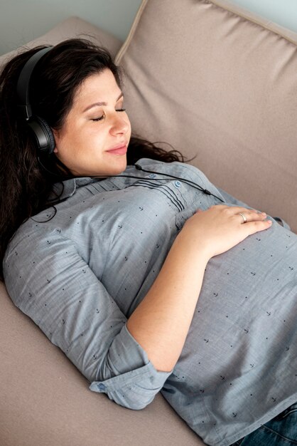 Schwangere Frau mit den Kopfhörern, die auf die Couch legen