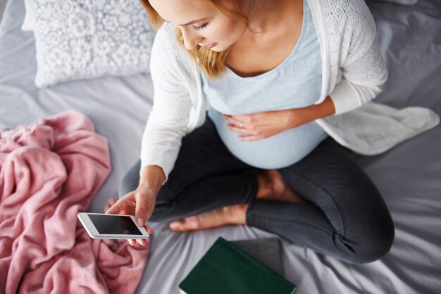 Schwangere Frau mit Handy im Schlafzimmer