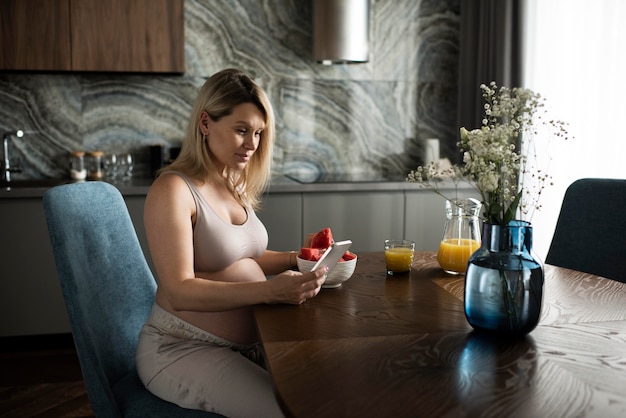 Schwangere Frau mit mittlerer Aufnahme, die am Tisch sitzt