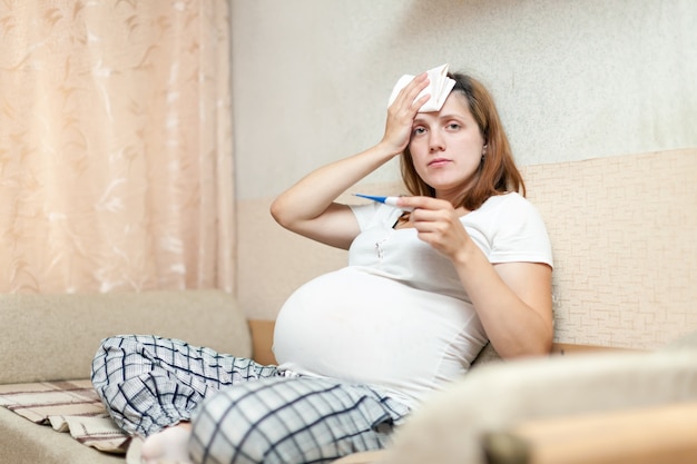 Schwangere frau mit thermometer im wohnzimmer