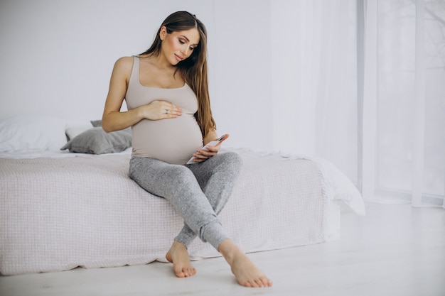 Schwangere Frau mit Ultraschallfoto auf dem Bett sitzend