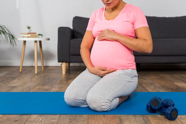 Schwangere Frau zu Hause mit Gewichten und Trainingsmatte