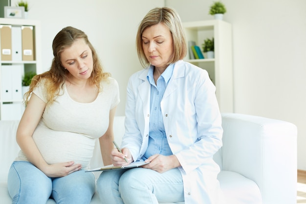 Schwangere Frau zu ihrem Arzt in einem Raum im Gespräch