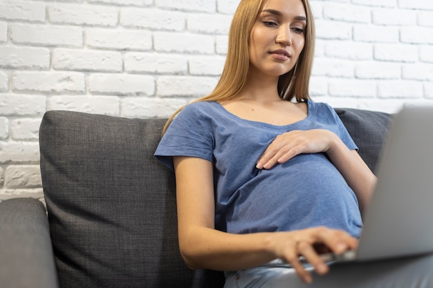 Schwangere Geschäftsfrau, die am Laptop von der Couch arbeitet