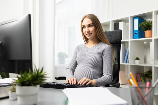 Schwangere Geschäftsfrau, die an ihrem Schreibtisch am Computer arbeitet