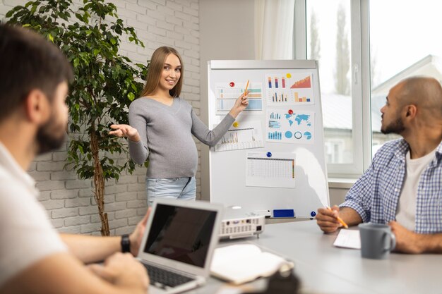 Schwangere Geschäftsfrau, die männlichen Mitarbeitern im Büro eine Präsentation gibt