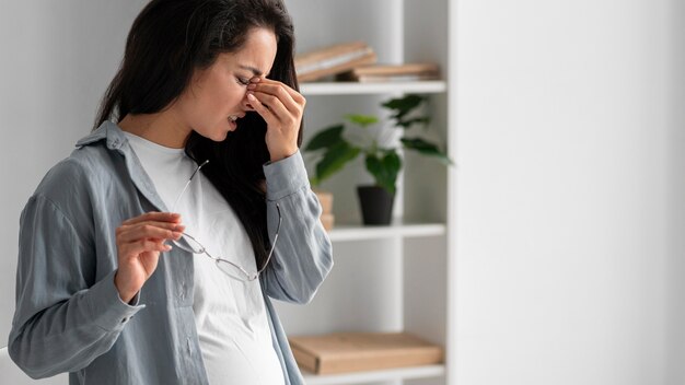 Schwangere Geschäftsfrau, die zu Hause wegen Kopfschmerzen ihre Brille abnimmt