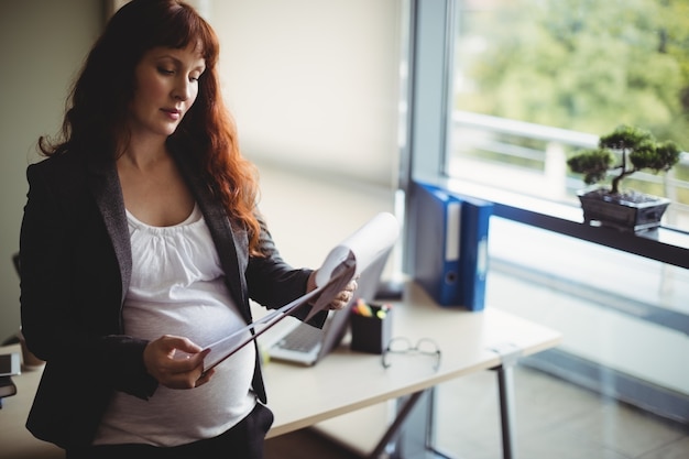 Schwangere Geschäftsfrau liest Papierdokumente