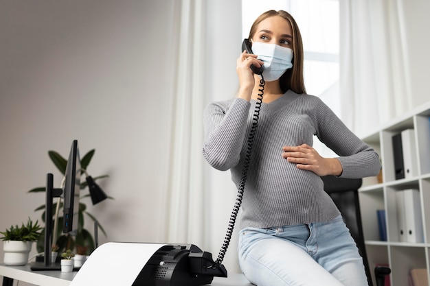 Kostenloses Foto schwangere geschäftsfrau mit medizinischer maske, die anrufe im büro entgegennimmt