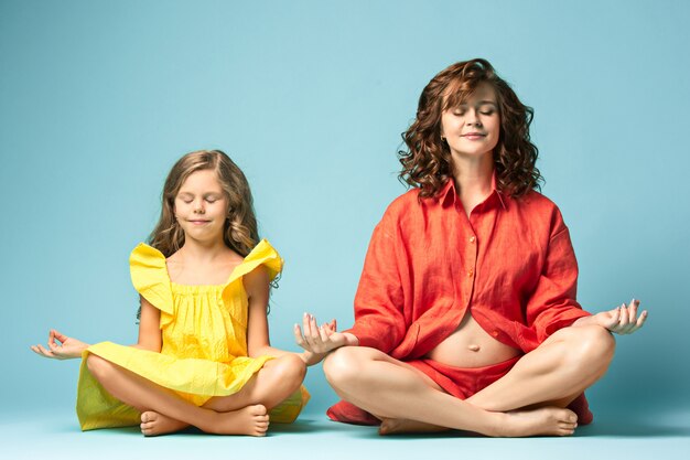 Schwangere Mutter mit jugendlich Tochter. Familienstudio-Porträt über blauem Hintergrund