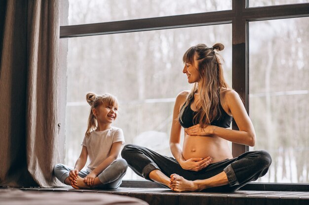 Schwangerer Mopther, der Yoga mit kleiner Tochter tut