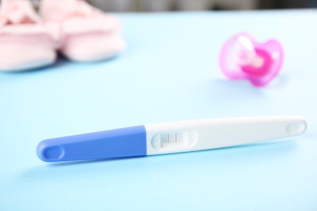 Schwangerschaftstest, babyschuhe und schnuller auf hellblauem hintergrund. baby born konzept