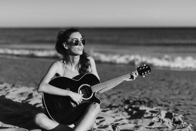 Kostenloses Foto schwarz-weiß-bild von mädchen gitarre spielen am strand