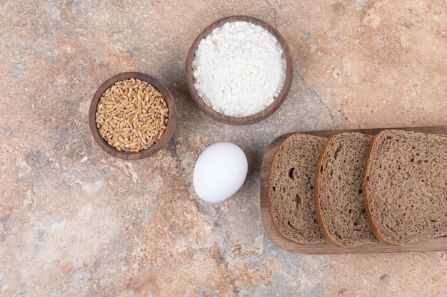 Schwarzbrotscheiben, Mehl, Gerste und Eier auf Marmoroberfläche