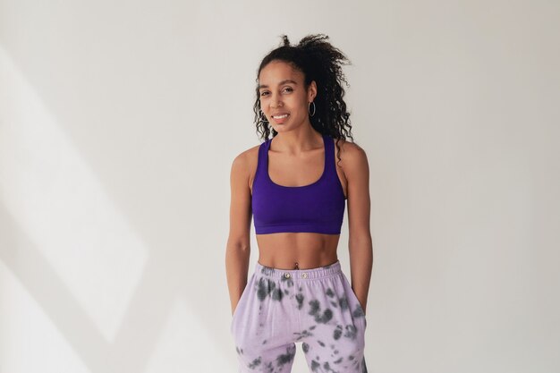 Schwarze Afroamerikanerin im stylischen Hipster-Fitness-Outfit violettes Top und Hose auf Weiß