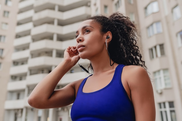 Schwarze Afroamerikanerin in Sport-Fitness-Stadtoutfit auf dem Dach, die trainieren, Musik über Kopfhörer zu hören?