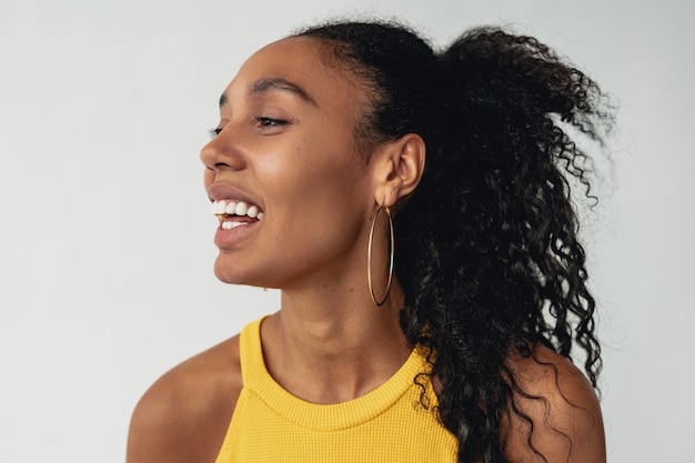 Schwarze afroamerikanische frau in stylischem hipster-outfit gelbes top auf weißem, isoliertem hintergrund., sommermodetrend, glücklich lächelnde ohrringe für lockiges haar Kostenlose Fotos