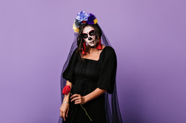 Schwarze Braut, die rote Rose hält. Porträt des Modells mit erschreckendem Make-up an Halloween.