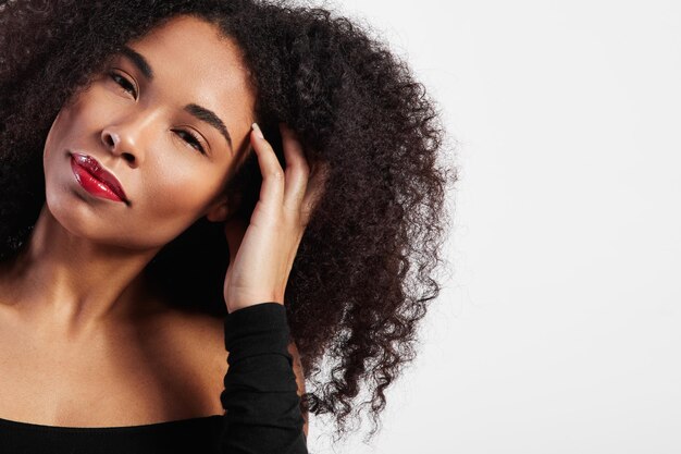 Schwarze Frau mit Afrohaar berührt es und schaut in die Kamera