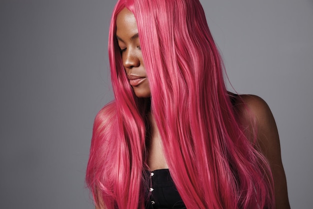 Schwarze Frau mit langem, glänzendem, glattem, rosafarbenem Haar, kreativem Haar in Salonfarbe
