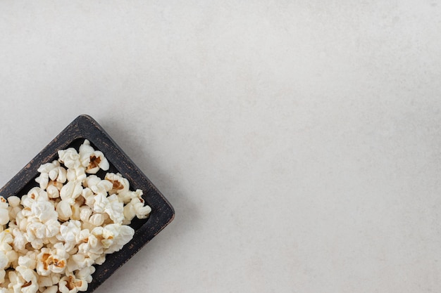 Schwarze holzplatte mit knusprigem popcorn auf marmortisch.