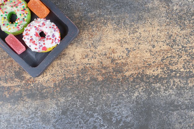 Schwarze Holzplatte mit mundgerechten Donuts und Marmeladen auf Holzoberfläche