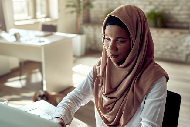 Schwarze islamische Geschäftsfrau, die Computer benutzt, während sie im Büro arbeitet