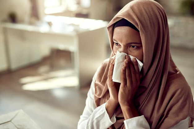Schwarze islamische Geschäftsfrau, die sich krank fühlt und die Nase weht, während sie im Büro arbeitet