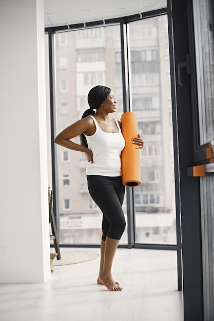 Schwarze junge Frau bereit zum Training mit orangefarbener Yogamatte