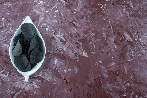 Schwarze kartoffelchips auf einem teller auf dem marmortisch.