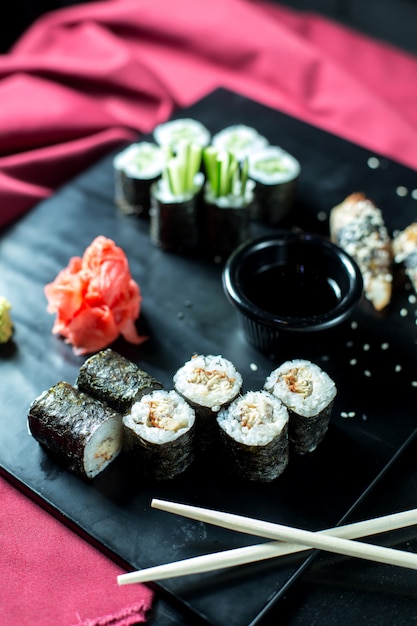 Schwarze Sushirollen mit Seitenansicht und Thunfisch, serviert mit Ingwer und Sojasauce auf einer Tafel