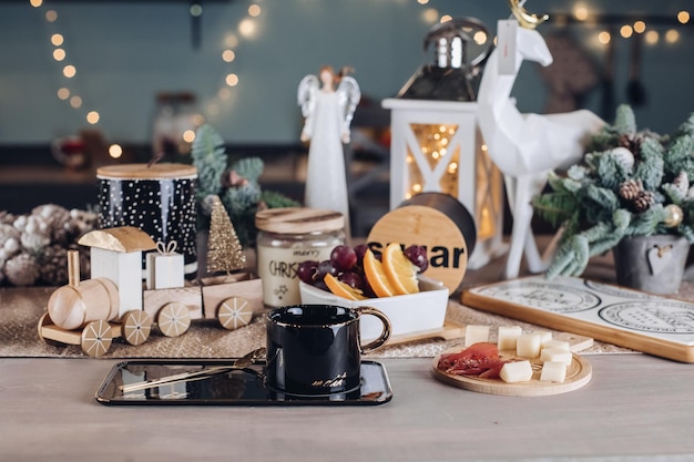 Schwarze Tasse, Essen und Neujahrsdekorationen stehen auf dem Tisch im Raum. Silvesterkonzept