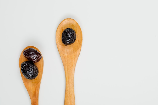 Schwarze und braune Oliven in einem Holzlöffel auf Weiß. Nahansicht.