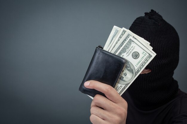 Schwarze Verbrecher tragen ein Hauptgarn, halten eine Dollarkarte auf Grau