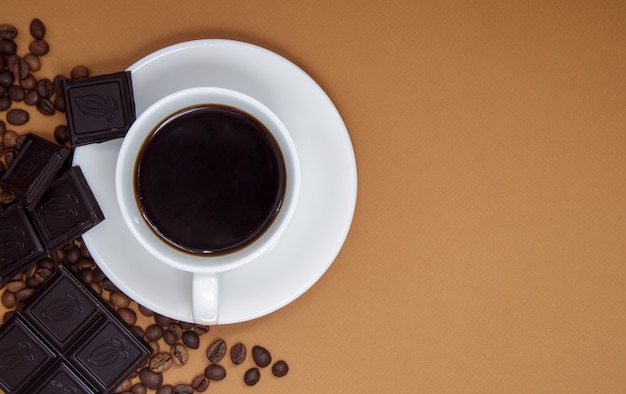 Schwarzer amerikanischer kaffee ohne milch in einer weißen tasse, schokolade und kaffeebohnen. ansicht von oben, flach, platz für text. eine tasse aromatischer morgenkaffee. schöner hintergrund für café, restaurantmenü.