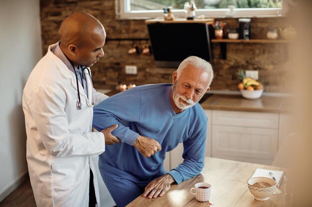 Schwarzer Arzt hilft Senioren beim Aufstehen vom Stuhl im Pflegeheim